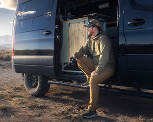 Man sitting inside a van in a desert landscape with mountains in the background